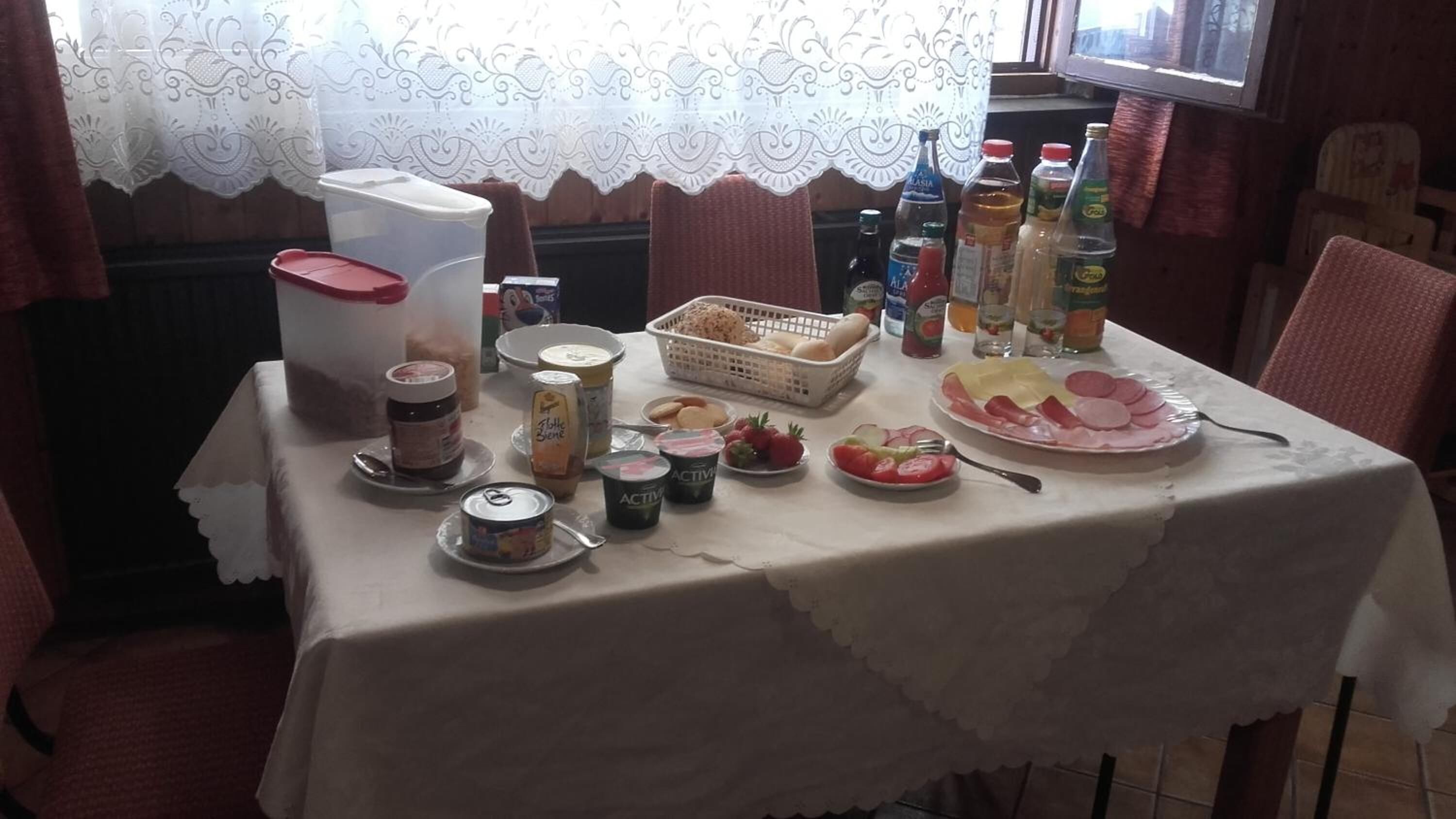 Una tavola imbandita con diversi cibi e condimenti, tra cui un cestino di pane, un piatto di salumi e diverse bottiglie di bevande.