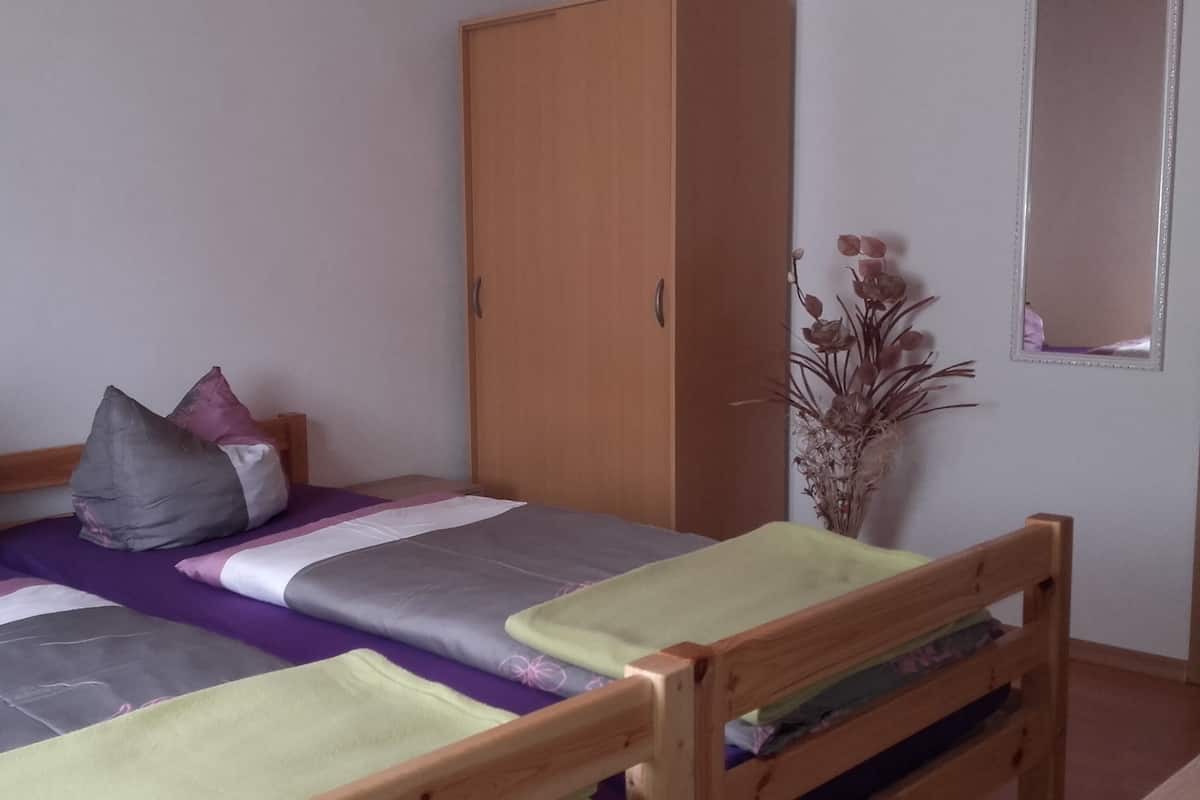 A single bed with a wooden headboard, a wooden wardrobe, and a mirror on the wall.