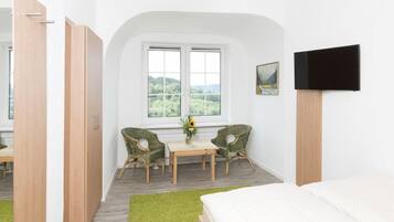 Un dormitorio con cama, televisión, ventana con vistas y una pequeña mesa con sillas.