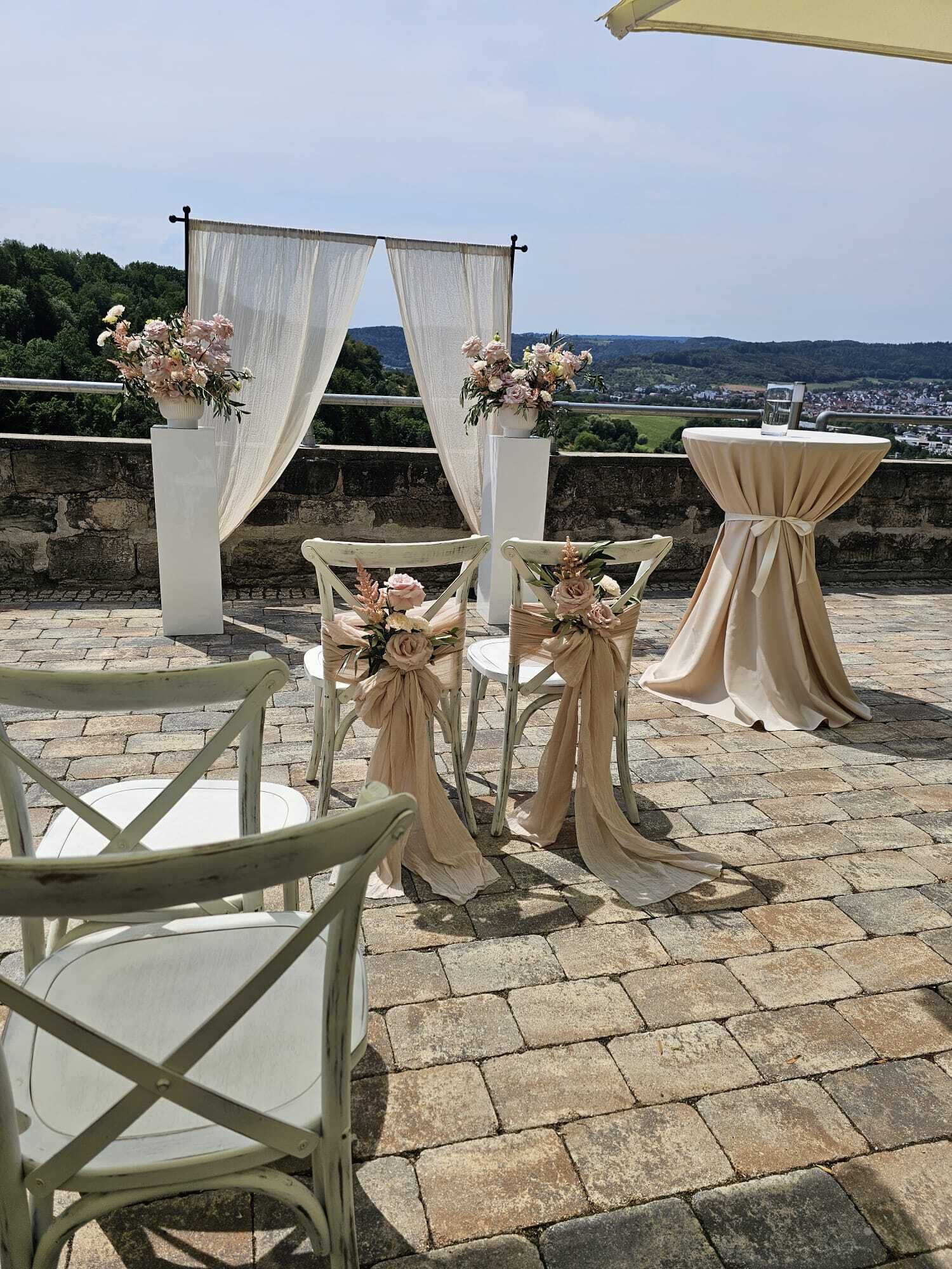 Terrasse mit Stühlen und Tischen, mit Stoff drapiert und mit Blumen geschmückt.