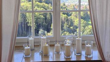 Una habitación con un ventanal amplio, sillas de madera y varias velas sobre un alféizar.