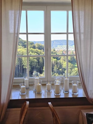 A room with a large window, wooden chairs, and multiple candles on a windowsill. - Hotel Garni BURG WALDENSTEIN (Rudersberg)