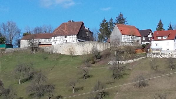 A traditional half-timbered building with a stone wall and a grassy hill. - Hotel Garni BURG WALDENSTEIN (Rudersberg)