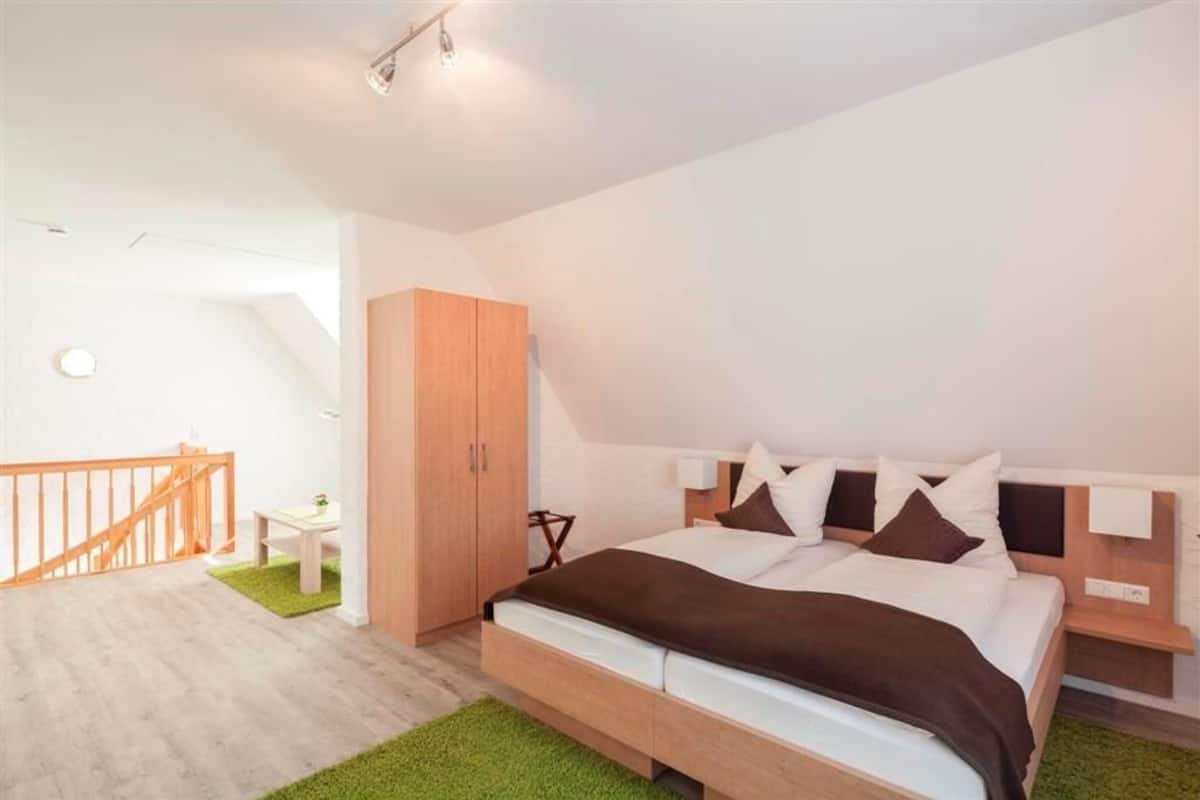 A modern bedroom with a large bed, wooden wardrobe, and a small desk.