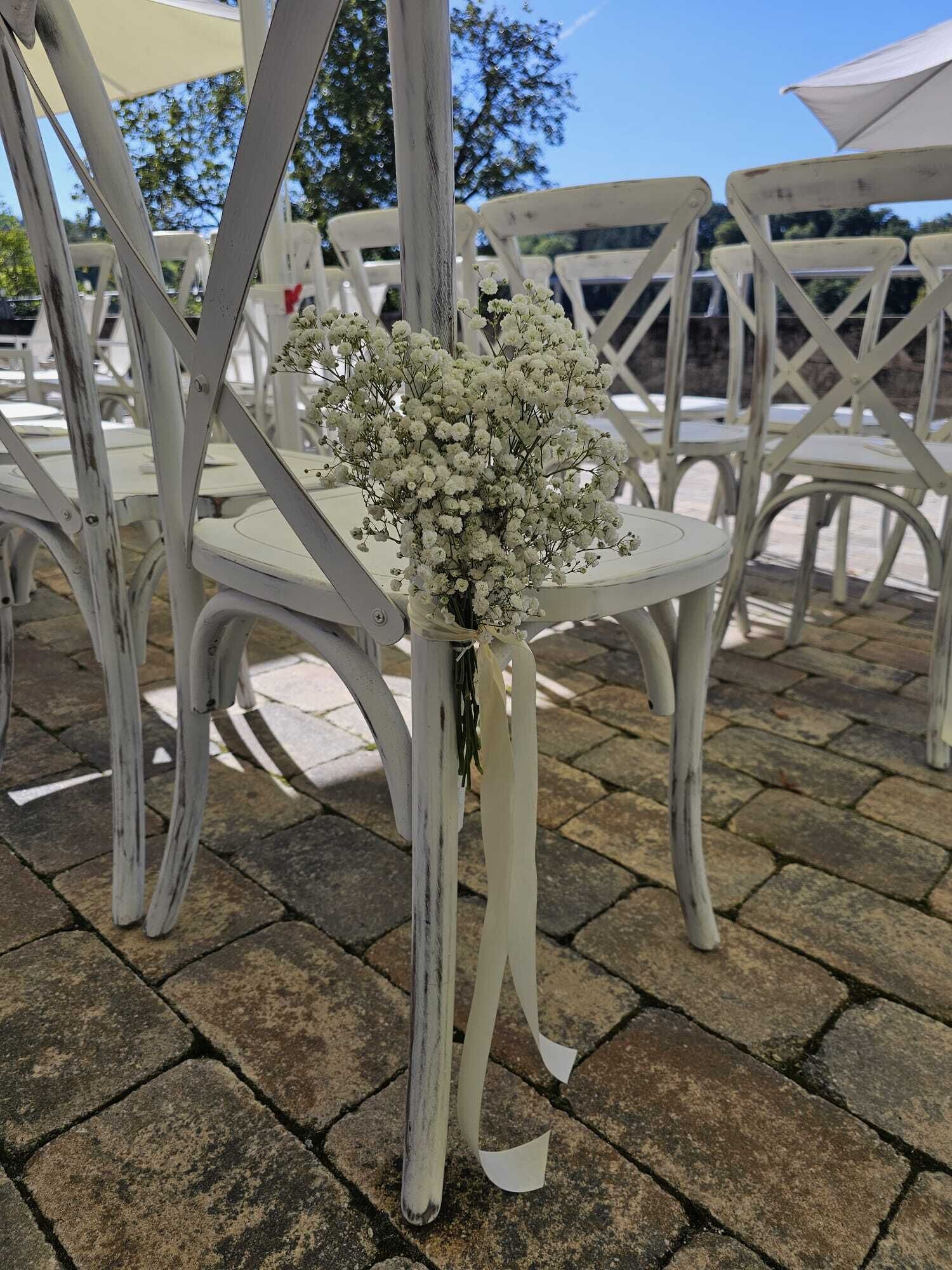 Une table en métal blanc, sur laquelle est disposé un bouquet de fleurs blanches, entourée de chaises en métal blanc.