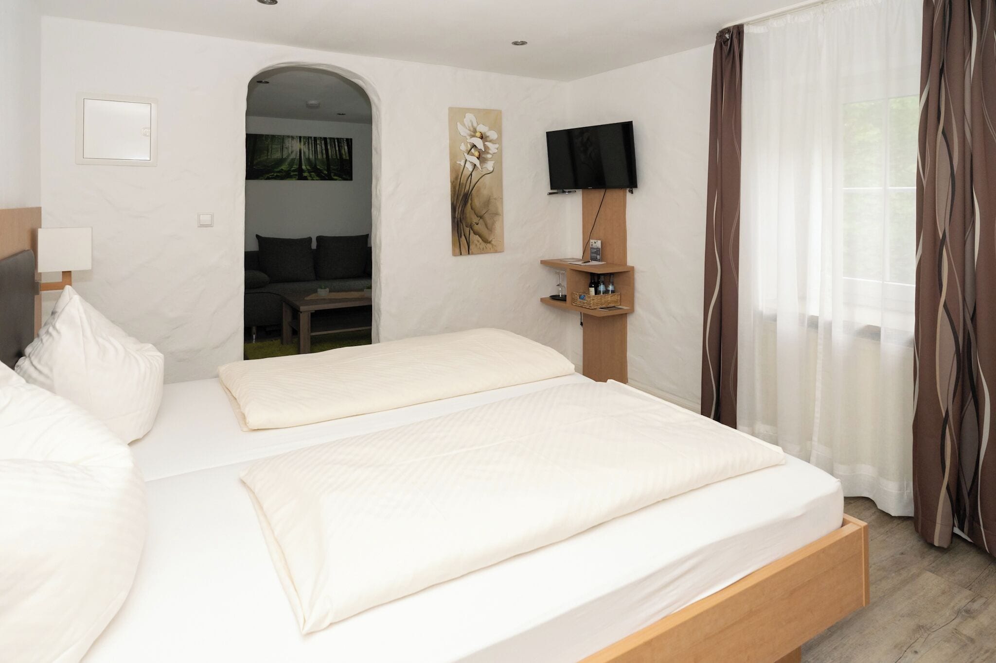 Habitación de hotel con una cama grande, televisión instalada en la pared, un pequeño rincón de estar y vistas al exterior.
