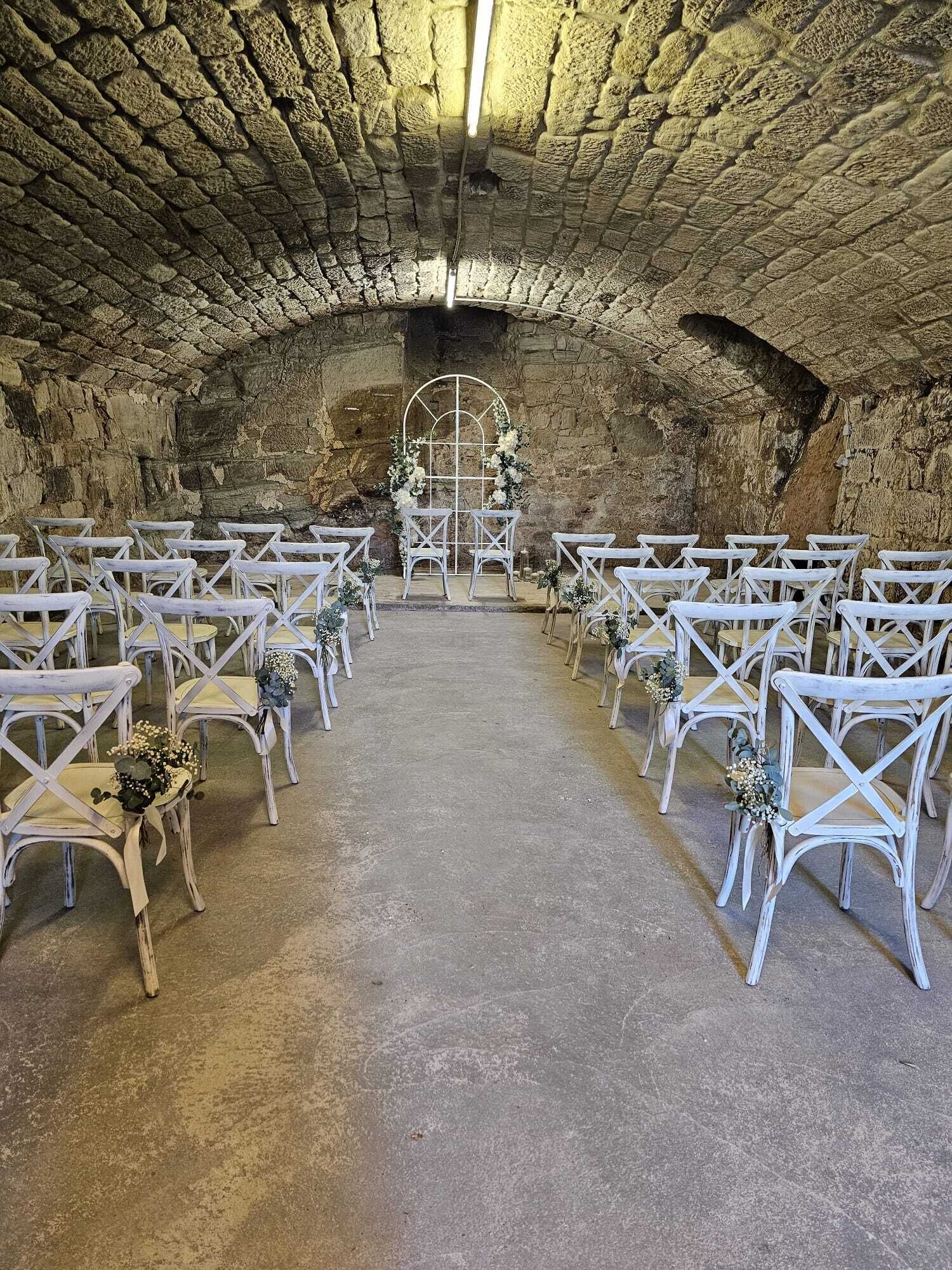 An arched stone room with white chairs and tables arranged for an event.