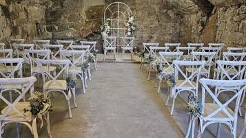 An arched stone room with white chairs and tables arranged for an event.