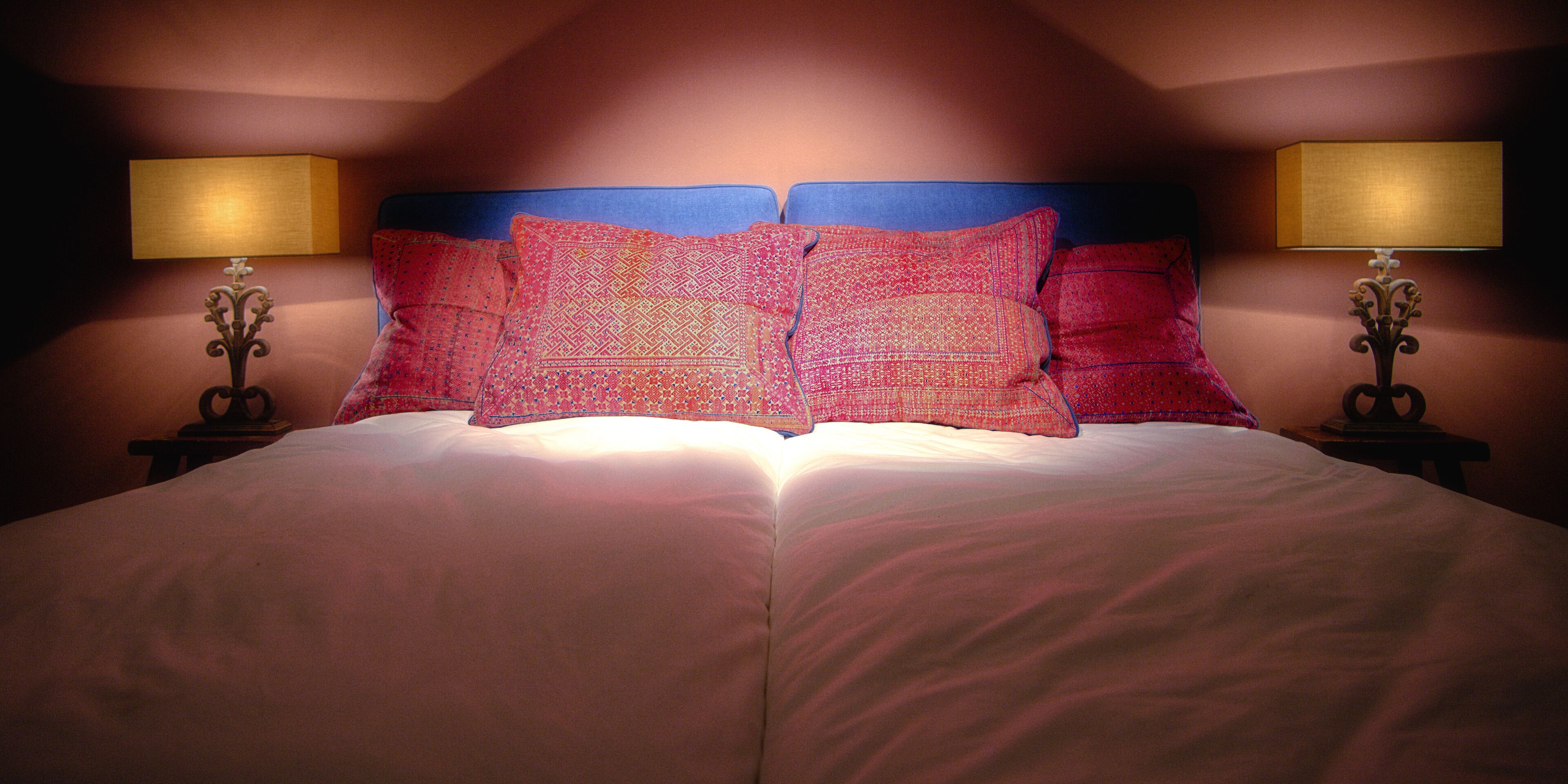 Una cama doble con cabecera azul y dos lámparas de noche.
