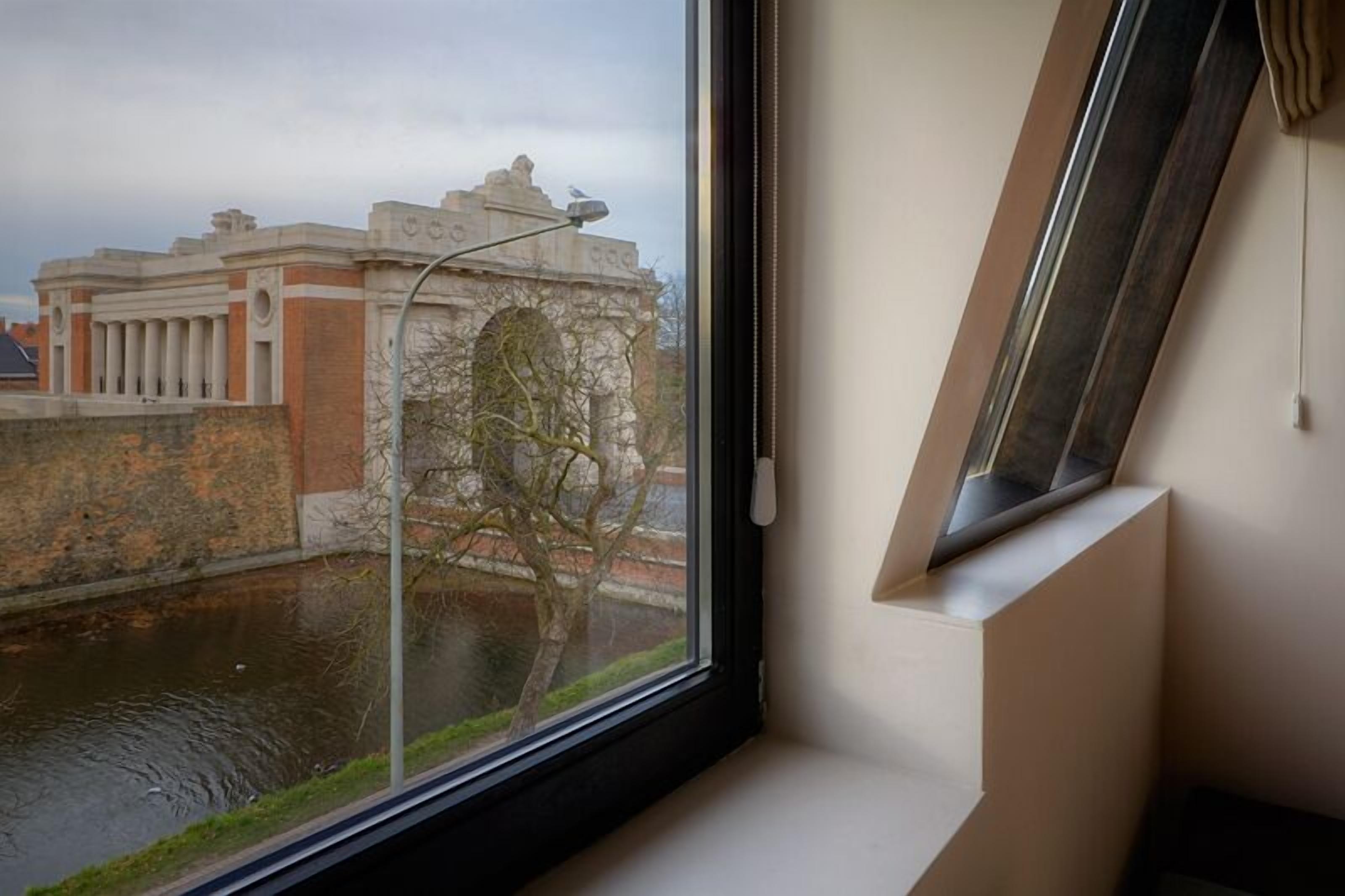 A room with a view of a historic building across a canal, a window with a curtain, and a modern light fixture.