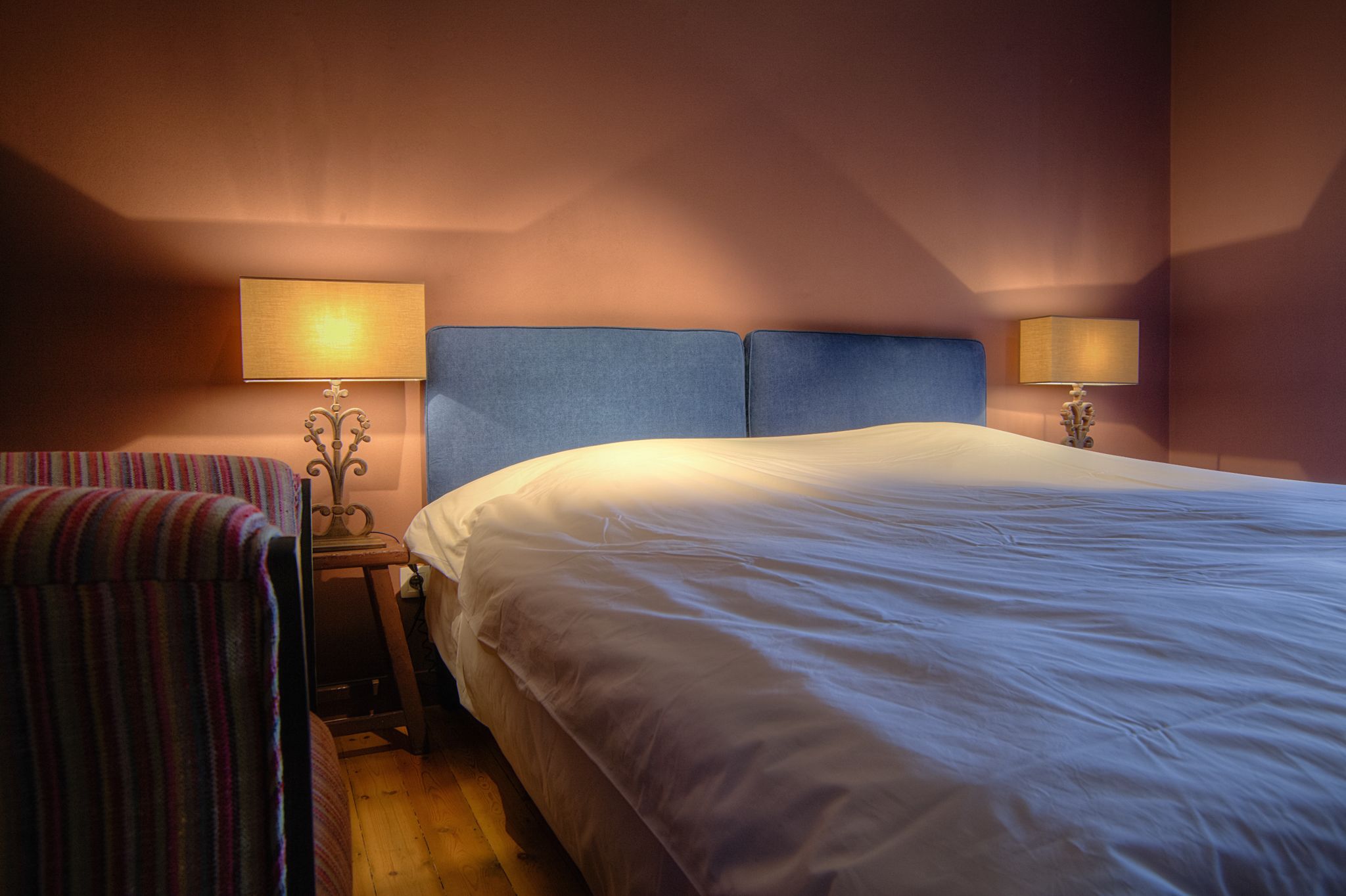 Une chambre d’hôtel avec un grand lit, deux lampes de chevet, une chaise à rayures et une petite table.