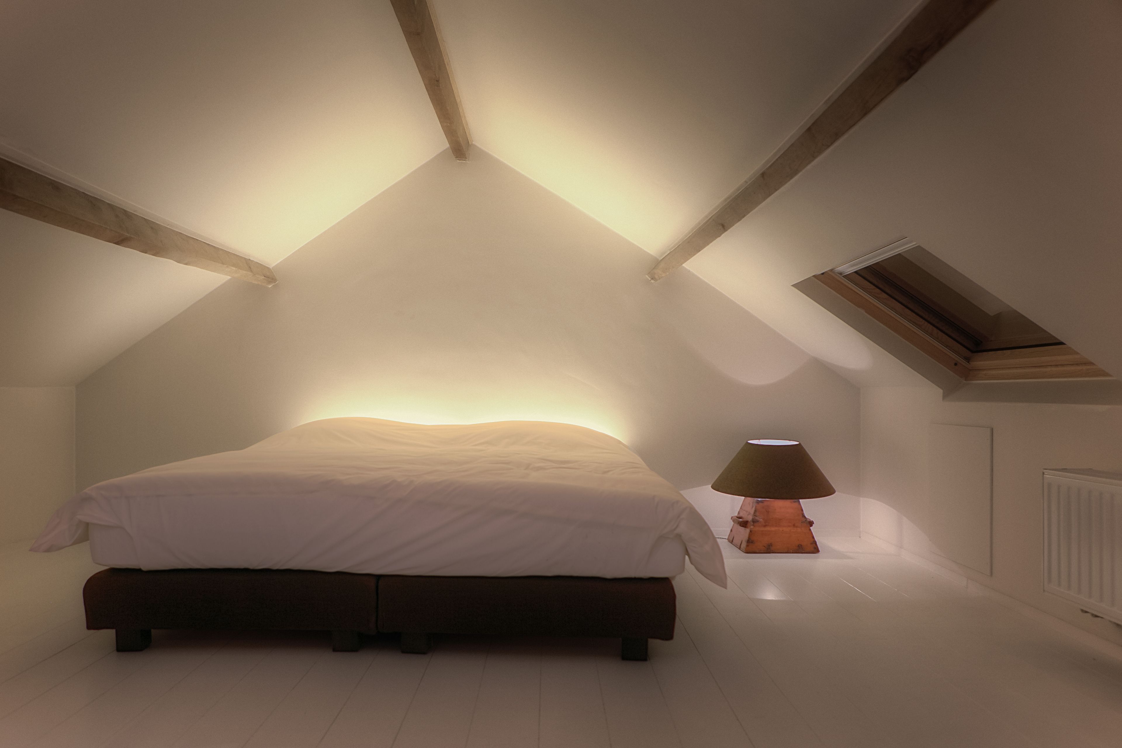 A bedroom with a sloped ceiling, a bed, a nightstand, and a lamp.