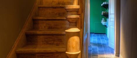 A wooden staircase with a handrail, leading to a room with a green wall and a tiled floor.