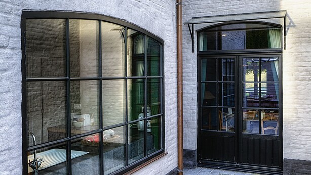 A building with large windows, a black door, and a tiled ground. - Menin Gate House  1 (Ypres)