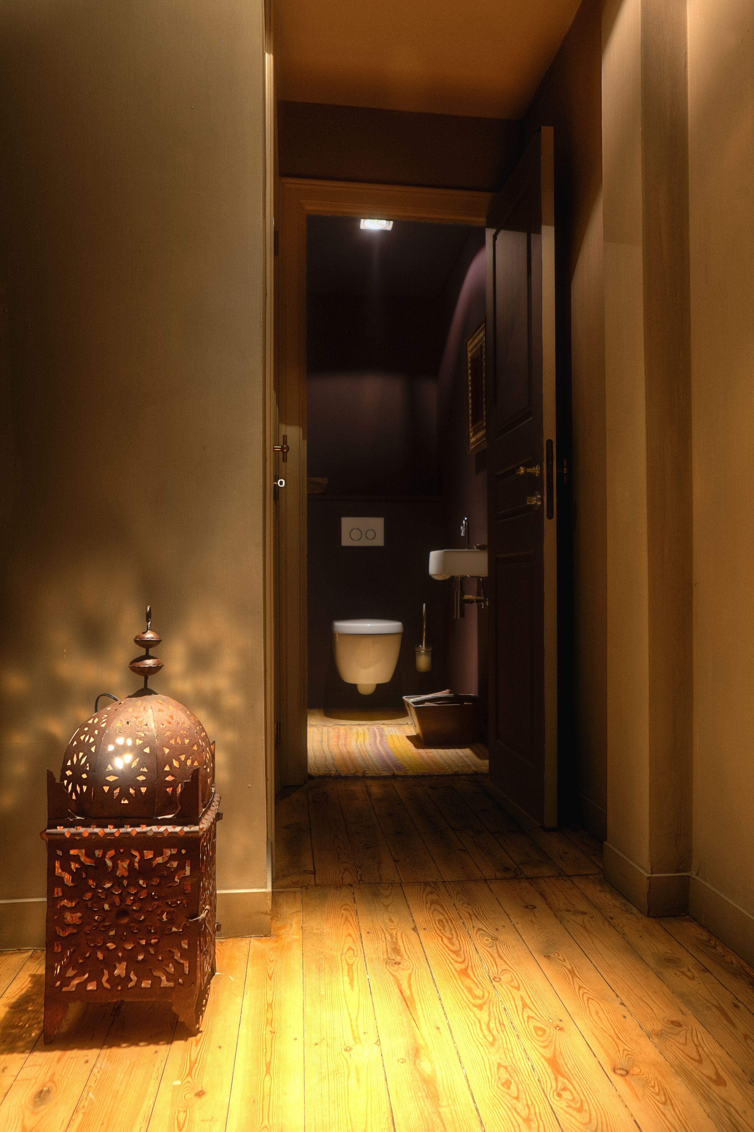 A narrow hallway with wooden flooring leading to a bathroom with a toilet and sink.