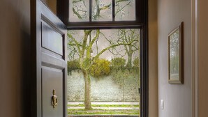 A hallway leading to a door with a view of a tree and a paved area outside. - Menin Gate House  1 (Ypres)
