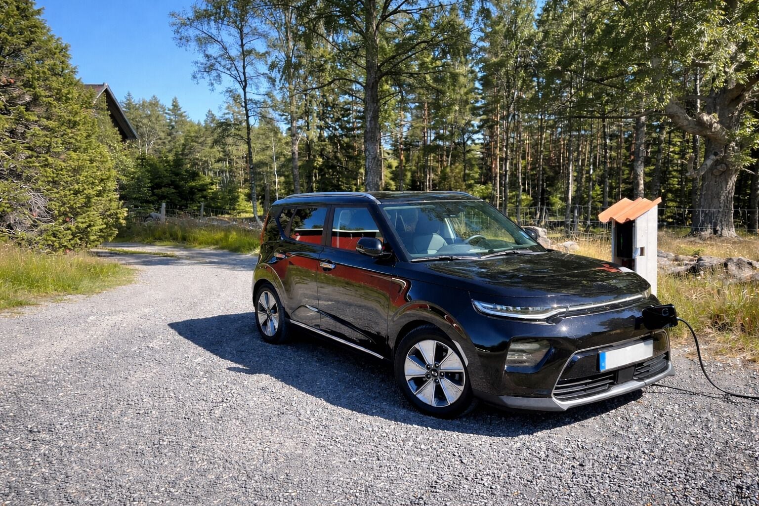 Un SUV negro estacionado en un camino de grava con un área boscosa al fondo.