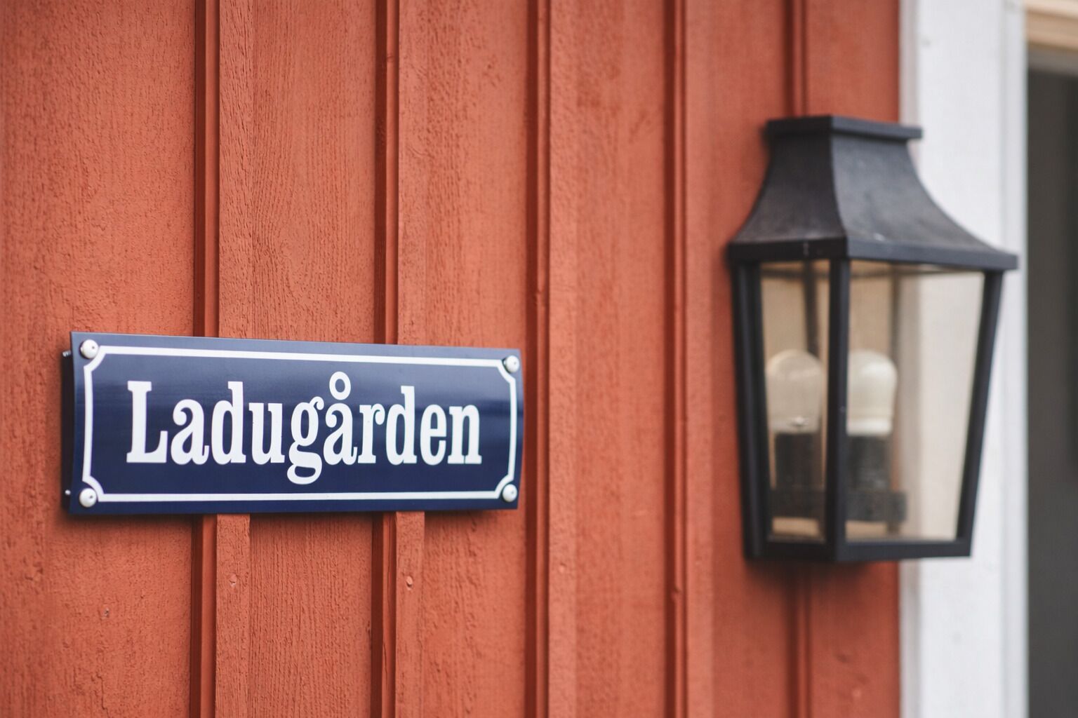 A sign reading "Ladugarden" mounted on a wooden wall, with a black lantern to the right.