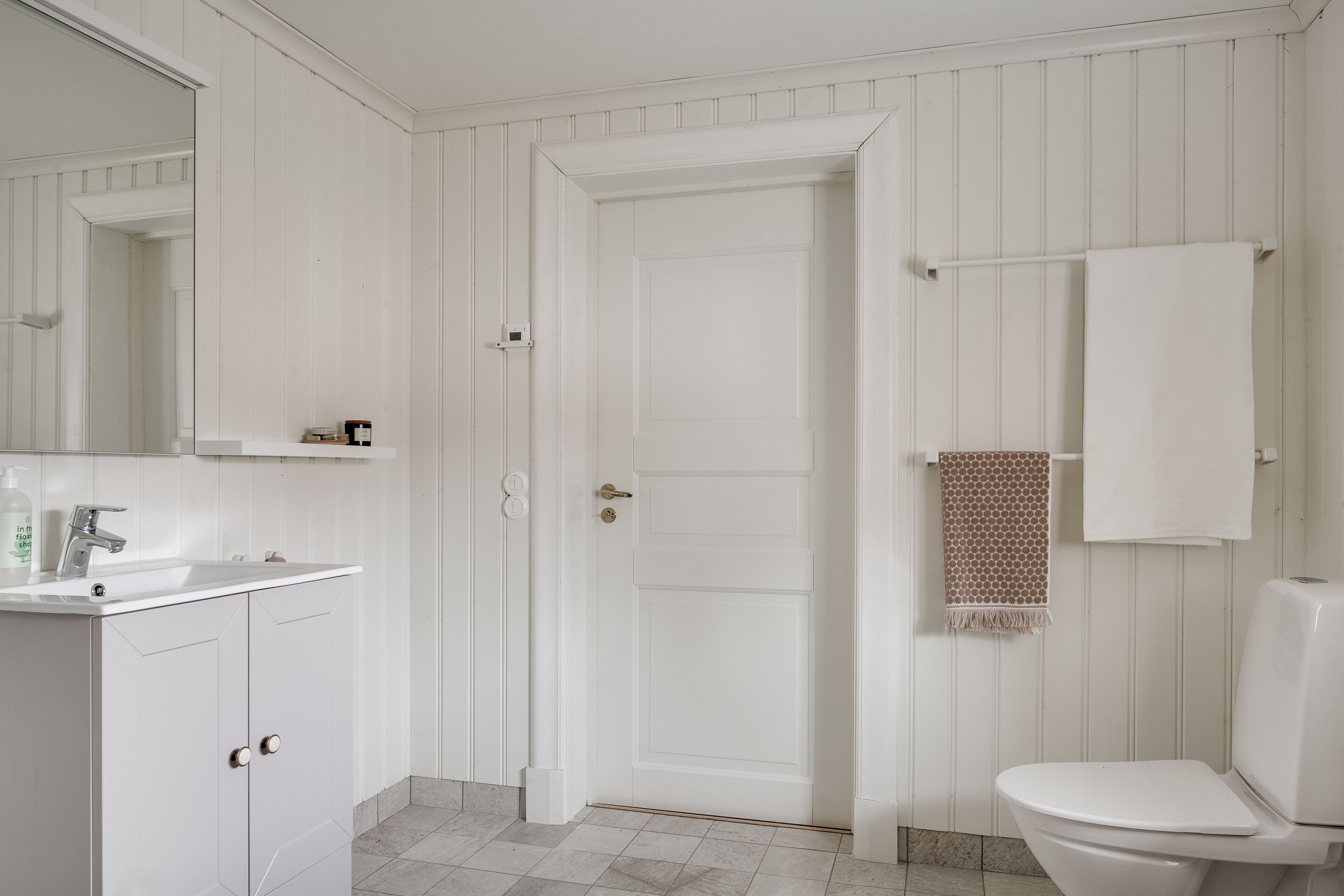 A bathroom with a white sink, mirror, and toilet. There is a towel rack with a patterned towel and a plain white towel.