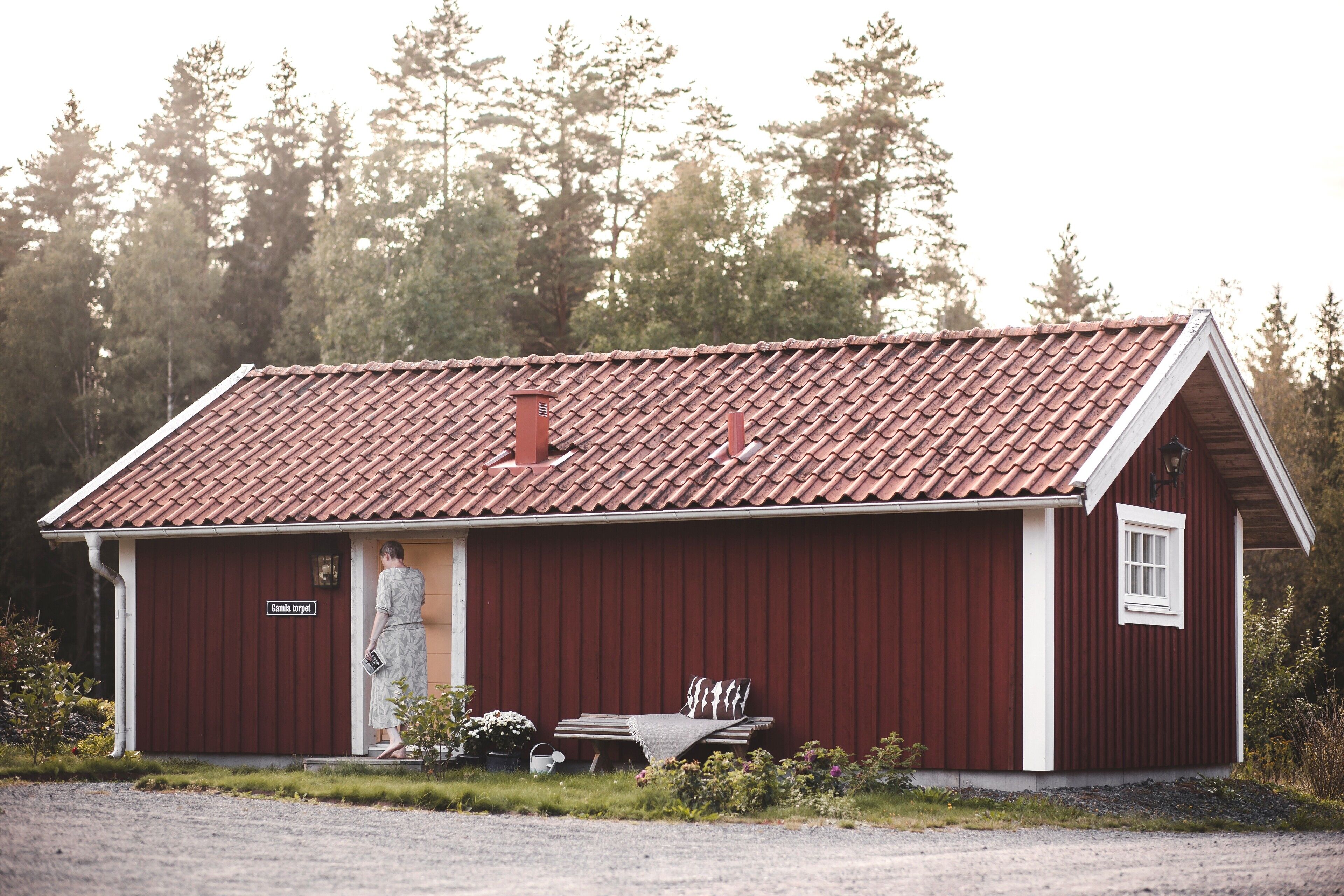 A red wooden building with a sloped roof, a bench outside, and a sign that reads "Gästehaus".
