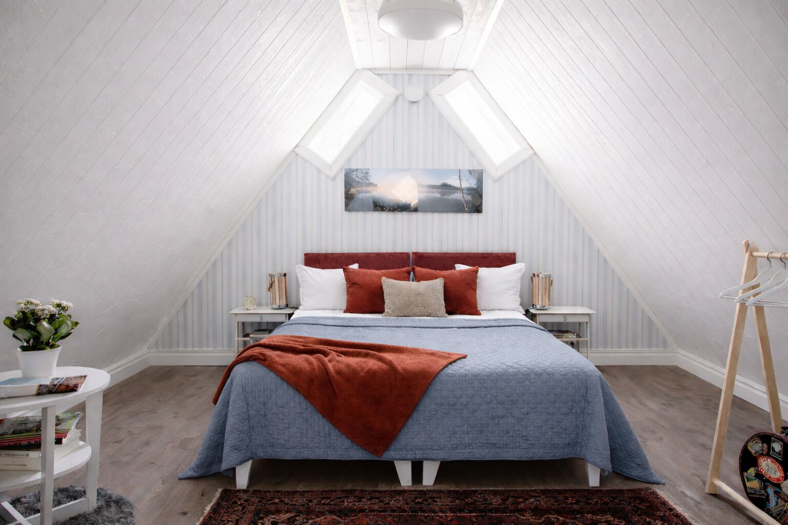 A bedroom with a sloped ceiling, a bed with a red headboard, white pillows, and a blue blanket.