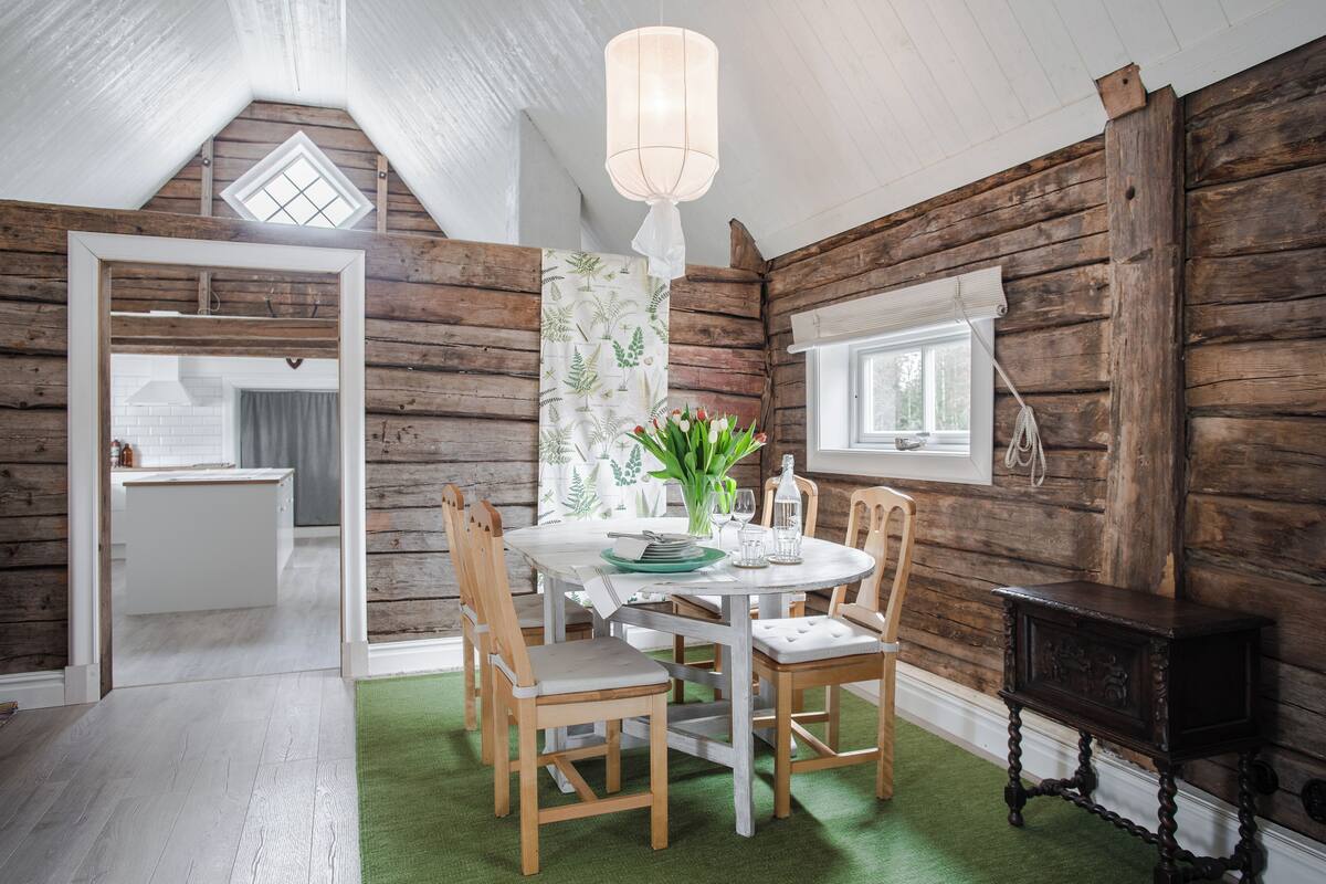A rustic dining area with a wooden table, chairs, and a green rug.