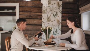 Una pareja sentada a una mesa redonda con mantel blanco, rodeada de paredes de madera y papel tapiz floral.