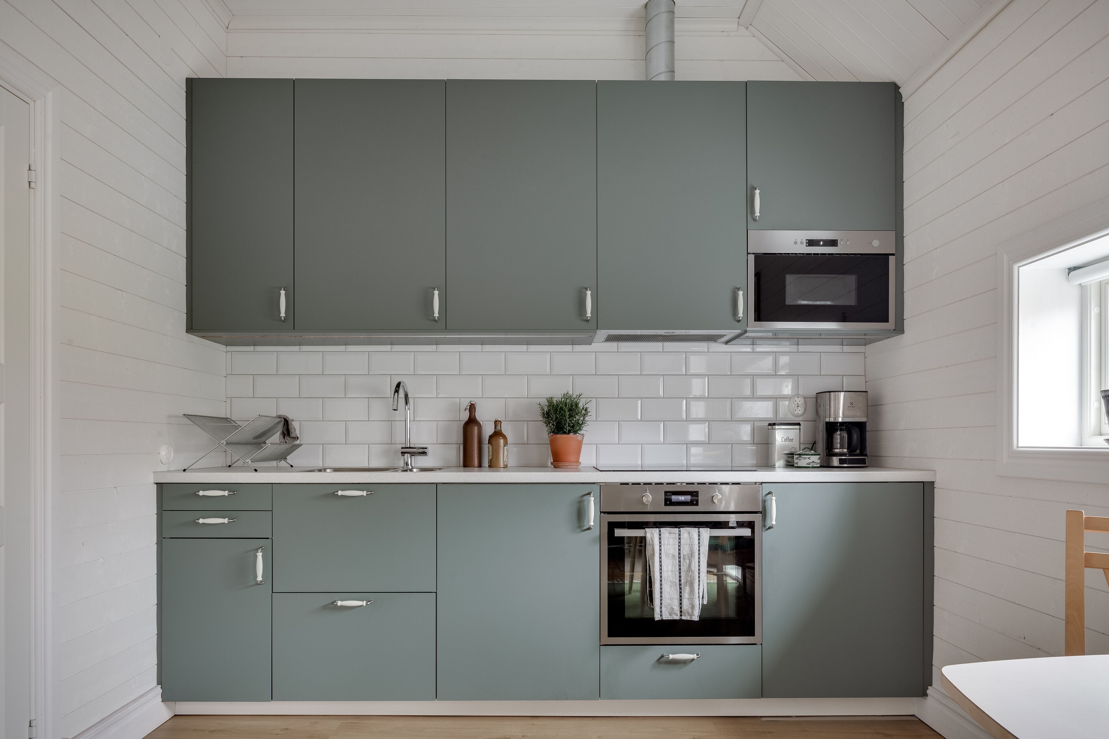 A modern kitchen with grey cabinets, white tiled backsplash, stainless steel appliances, and a wooden floor.