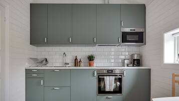 A modern kitchen with grey cabinets, white tiled backsplash, stainless steel appliances, and a wooden floor.