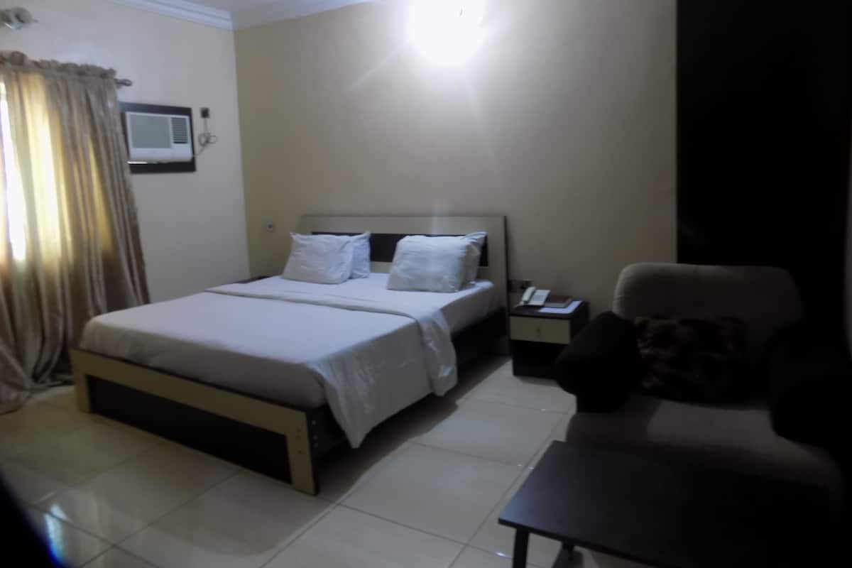 A hotel room with a bed, bedside table, chair, and a small table.