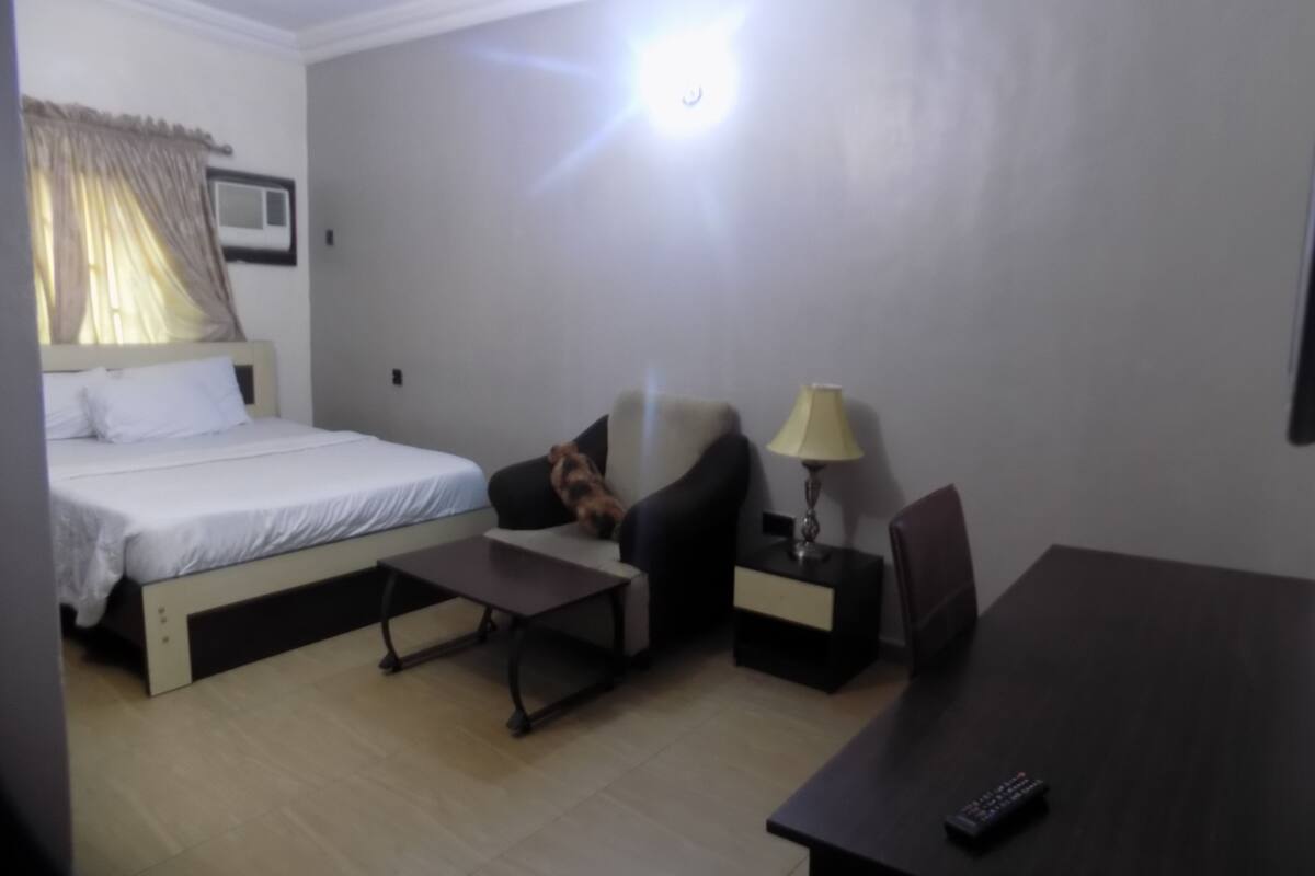 A hotel room with a bed, a sofa, a small table, a lamp, and a TV.