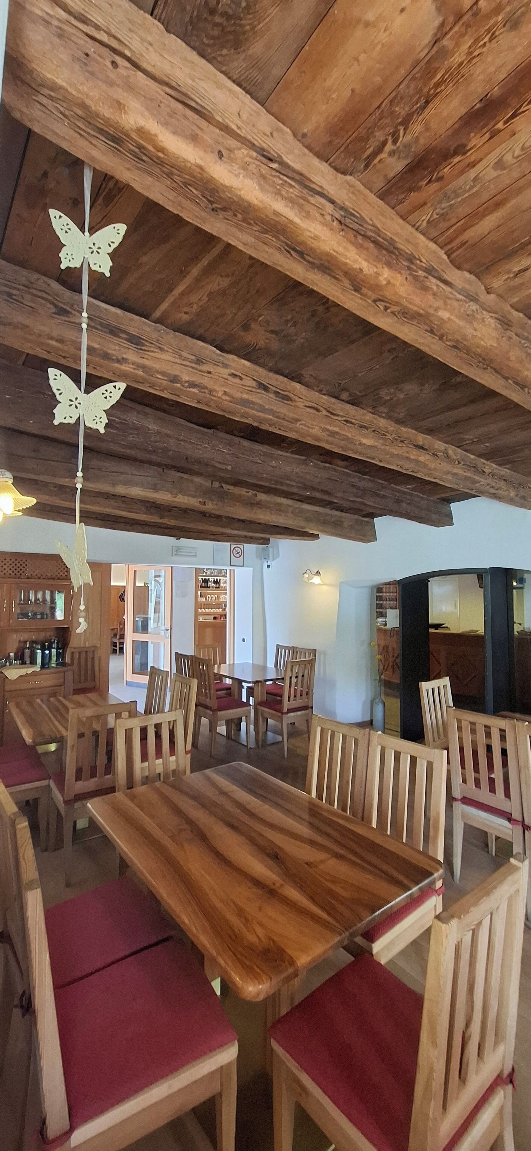 Un interno rustico con travi a vista in legno, un tavolo da pranzo centrale con sedie e una cucina in lontananza.