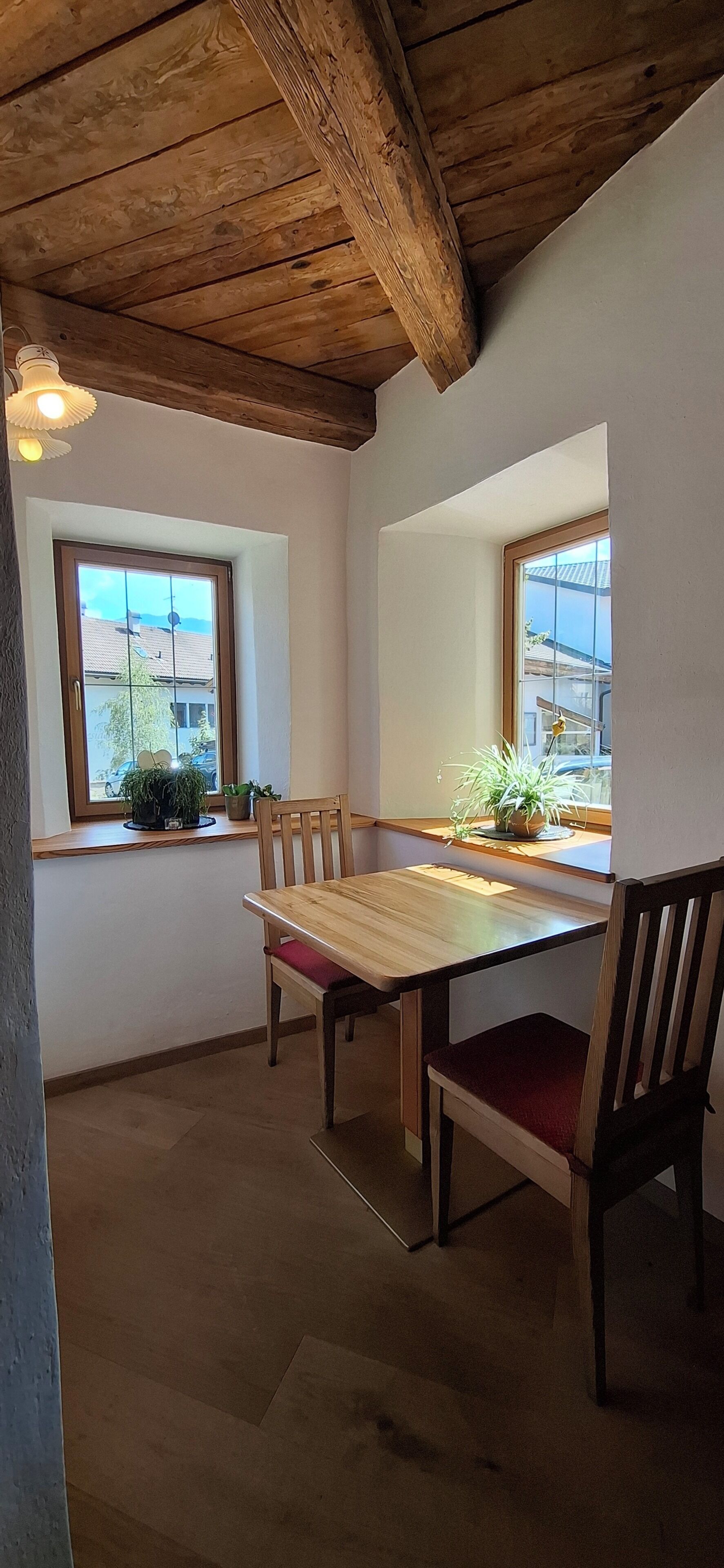 A dining area with a wooden table and chairs, a window with a view of buildings, and a ceiling with exposed beams.