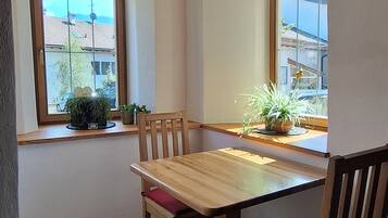A dining area with a wooden table and chairs, a window with a view of buildings, and a ceiling with exposed beams.