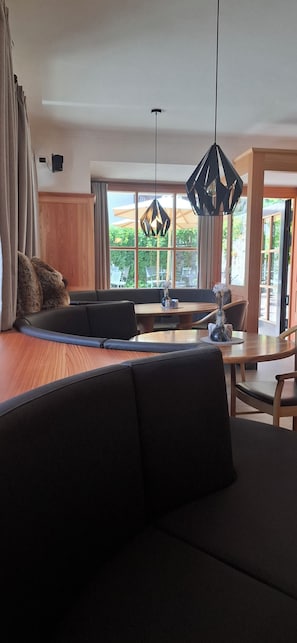 A modern living room with a sofa, a dining table, and a large window with a view of greenery. - Gasthof Zur Sonne (Laion)
