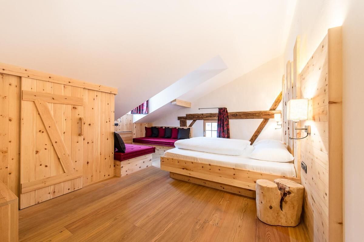 A wooden room with a loft bed, a wooden bench, and a small stool.