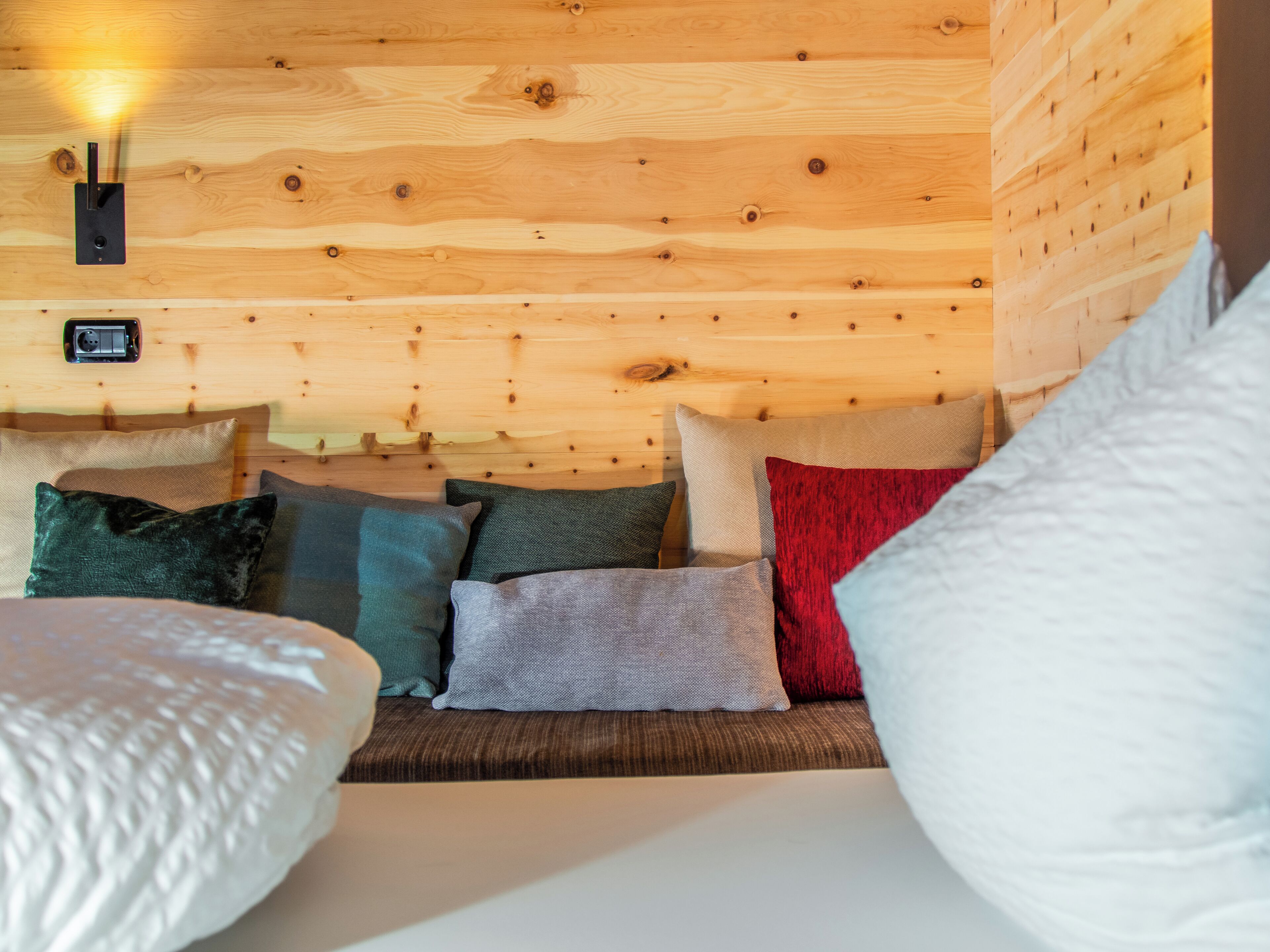 A wooden cabin interior with a bed, pillows, and a wall-mounted light fixture.