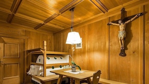 Un intérieur en bois, avec une croix en bois, une table et une étagère contenant des ustensiles de cuisine.