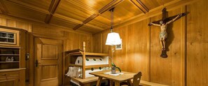 Un intérieur en bois, avec une croix en bois, une table et une étagère contenant des ustensiles de cuisine.