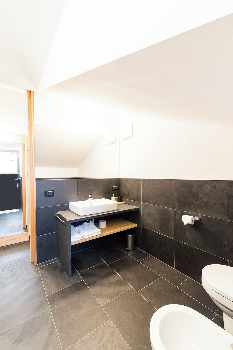 A modern bathroom with a large sink, dark tiles, and a wooden vanity.
