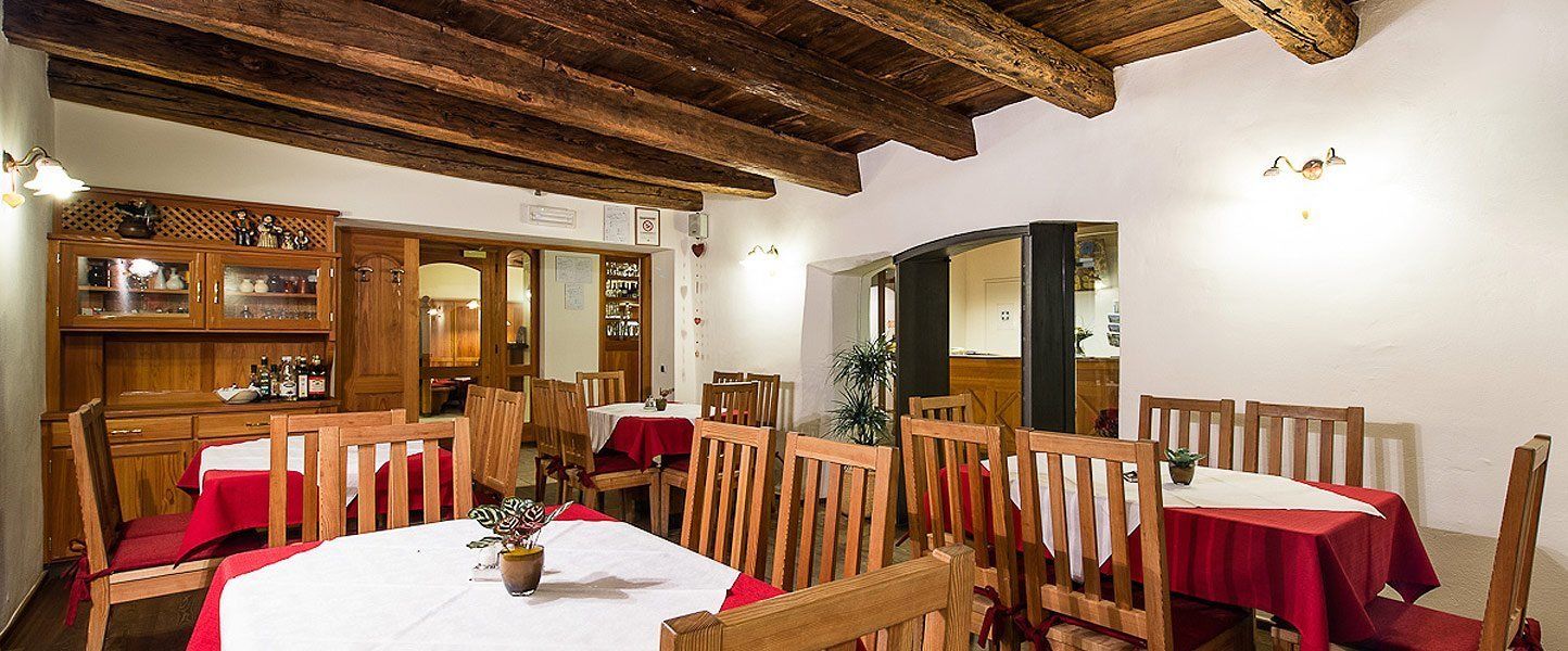A dining area with wooden tables and chairs, a wooden cabinet with glass doors, and a ceiling with exposed beams.