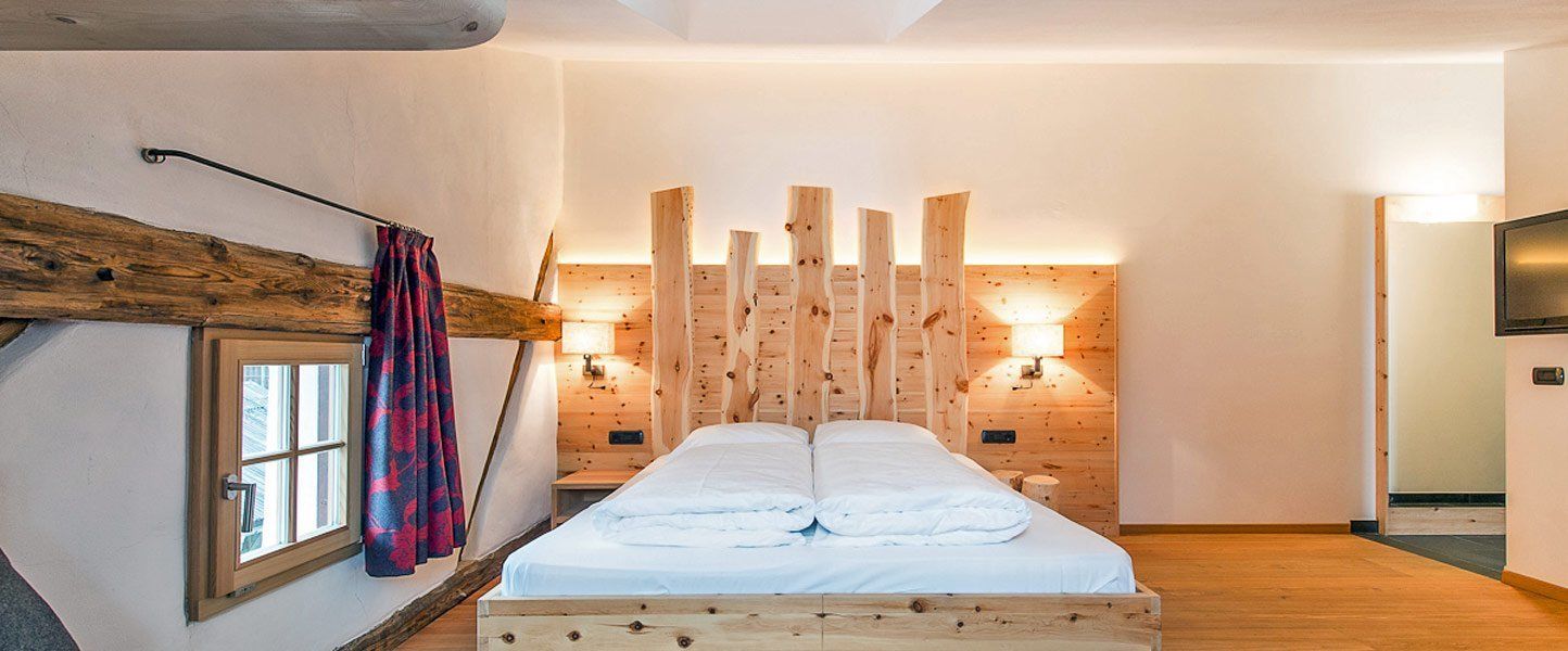 Un dormitorio acogedor con una cama de madera, una ventana con cortinas y un televisor montado en la pared.