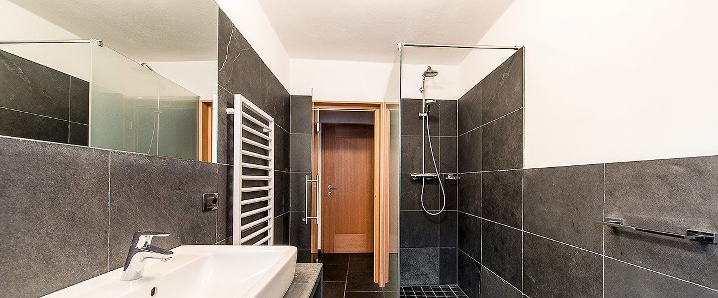 Un baño moderno con cabina de ducha de vidrio, bañera blanca y paredes con azulejos oscuros.