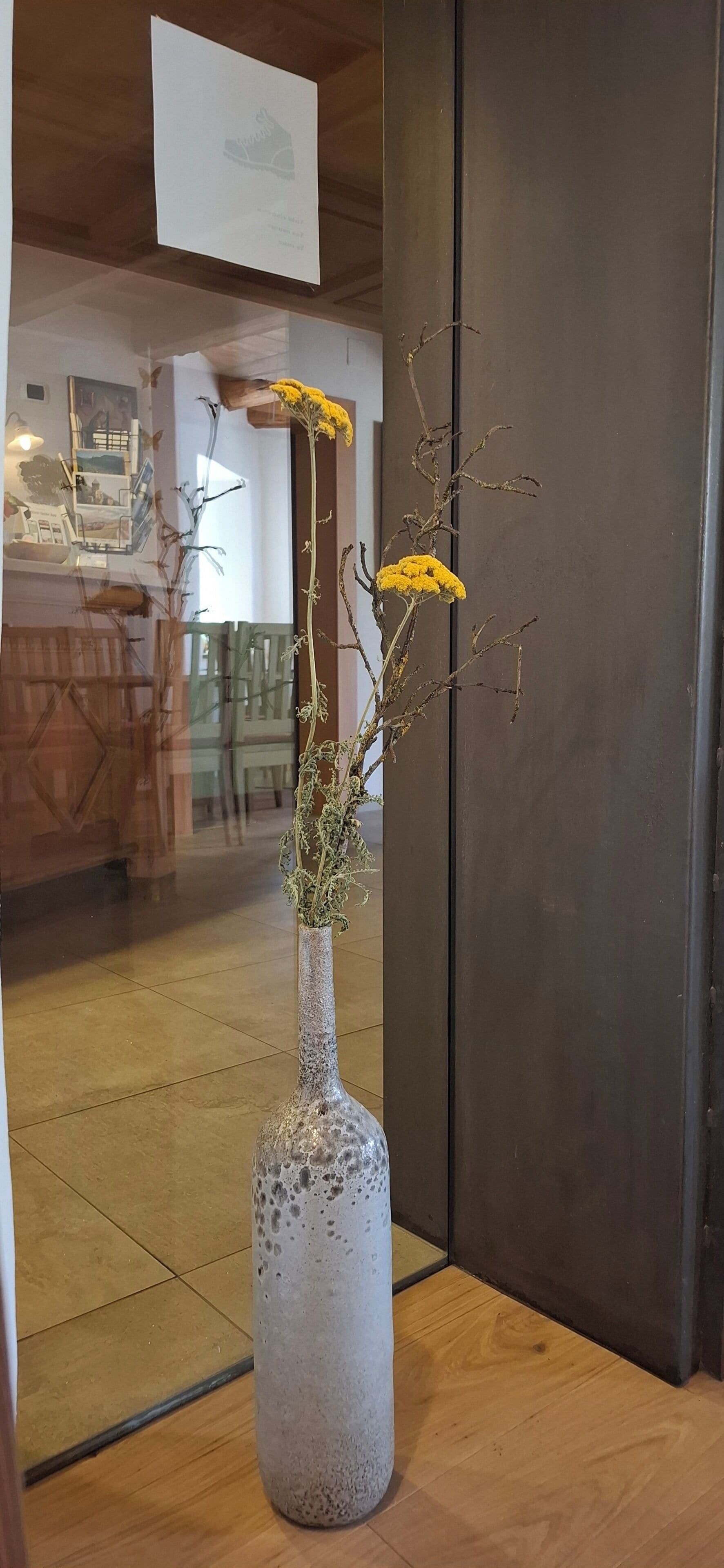 Un vase contenant des branches séchées et des fleurs jaunes, posé sur un plancher en bois.