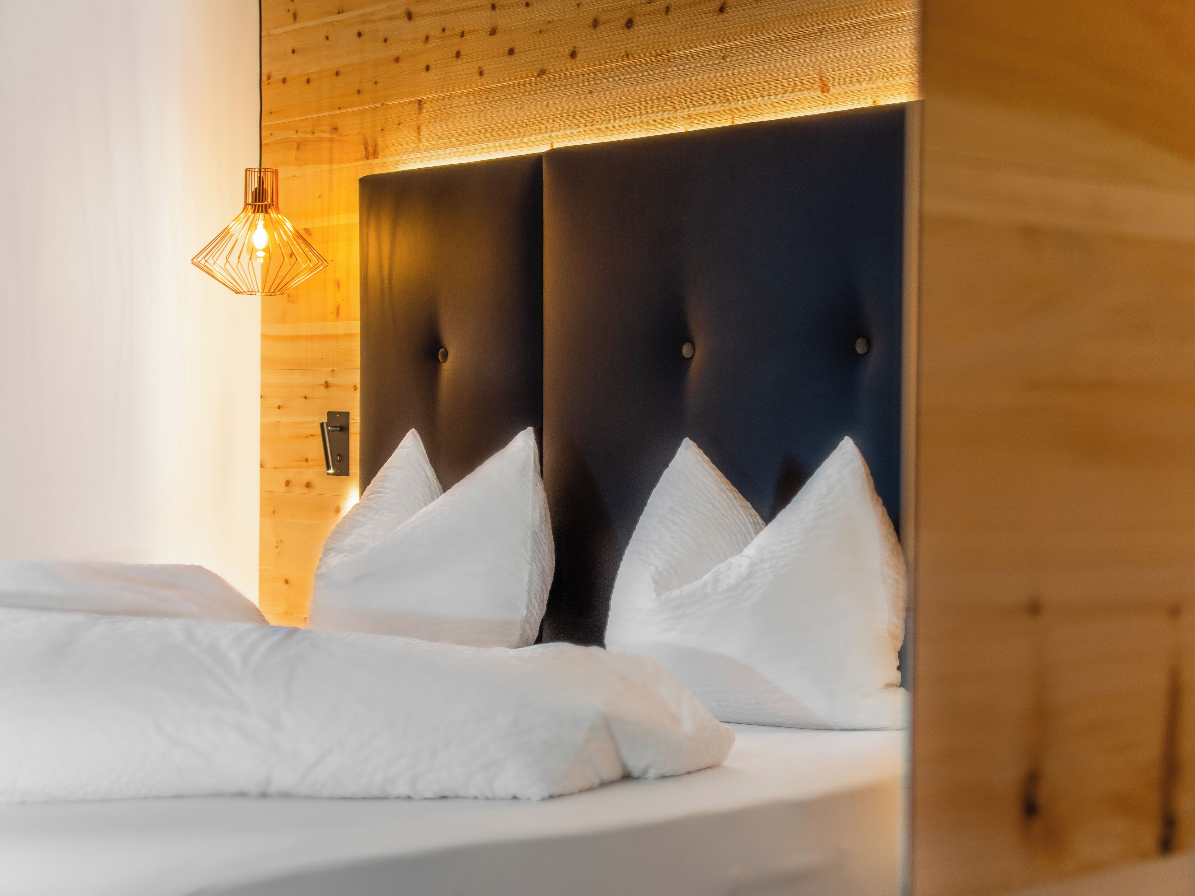 Una habitación de hotel con cabecera de madera, ropa de cama blanca y una lámpara colgante.