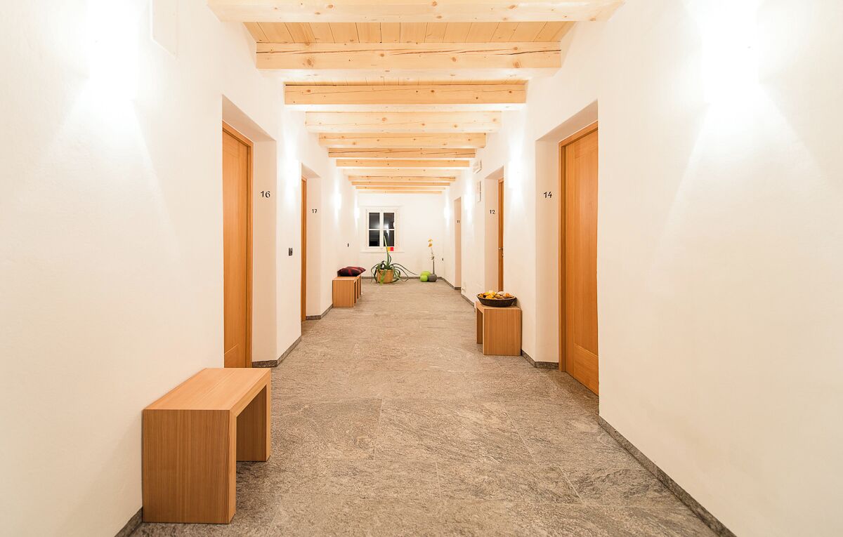 Un couloir avec des poutres en bois au plafond, des portes numérotées et un banc.