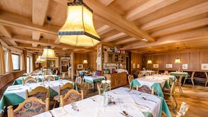 Un restaurant au décor intérieur en bois, avec de nombreuses tables recouvertes de nappes blanches et agrémentées de chemins de table verts, et des lampes suspendues.