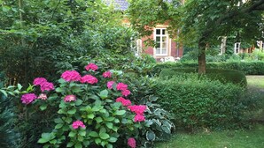 A lush garden with vibrant pink flowers and neatly trimmed hedges. - Hotel Cramer (Werlte)