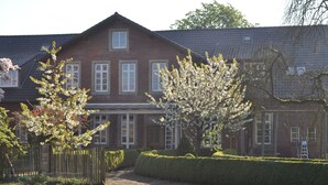 A large brick house with a symmetrical facade, multiple windows, and a well-maintained garden with trimmed hedges and flowering trees. - Hotel Cramer (Werlte)