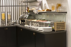 Una barra de buffet con diferentes opciones de comida, una máquina de café y salsas.
